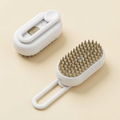 White pet grooming brush with beige bristles, shown from above and below on a cream background